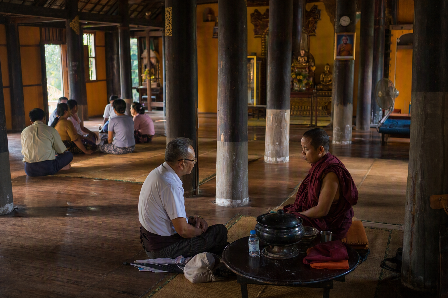 Monks and lay visitors during quiet daily activity inside a Marma Buddhist monastery