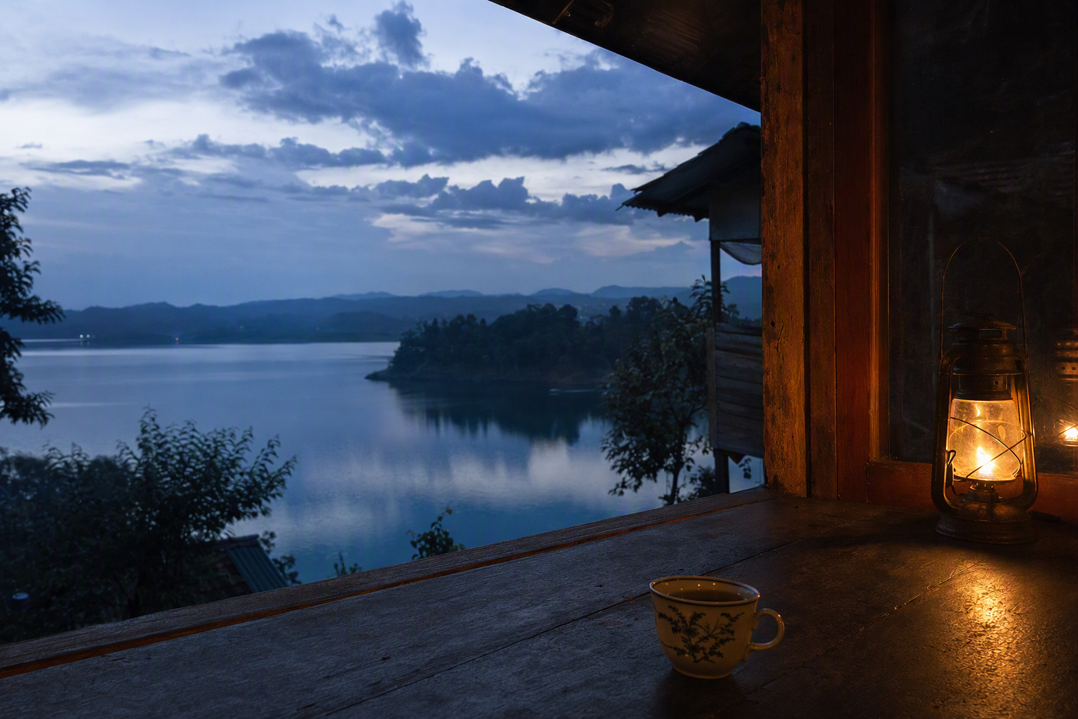 Blue-hour light across Kaptai Lake viewed from a weathered timber veranda