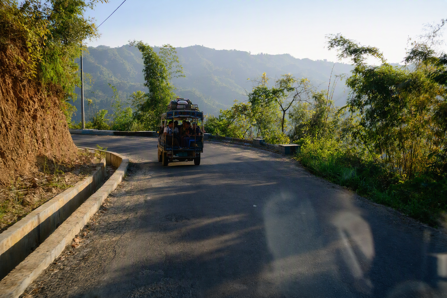 A shared vehicle rounding a bend on the Chimbuk hill road through dense green slopes