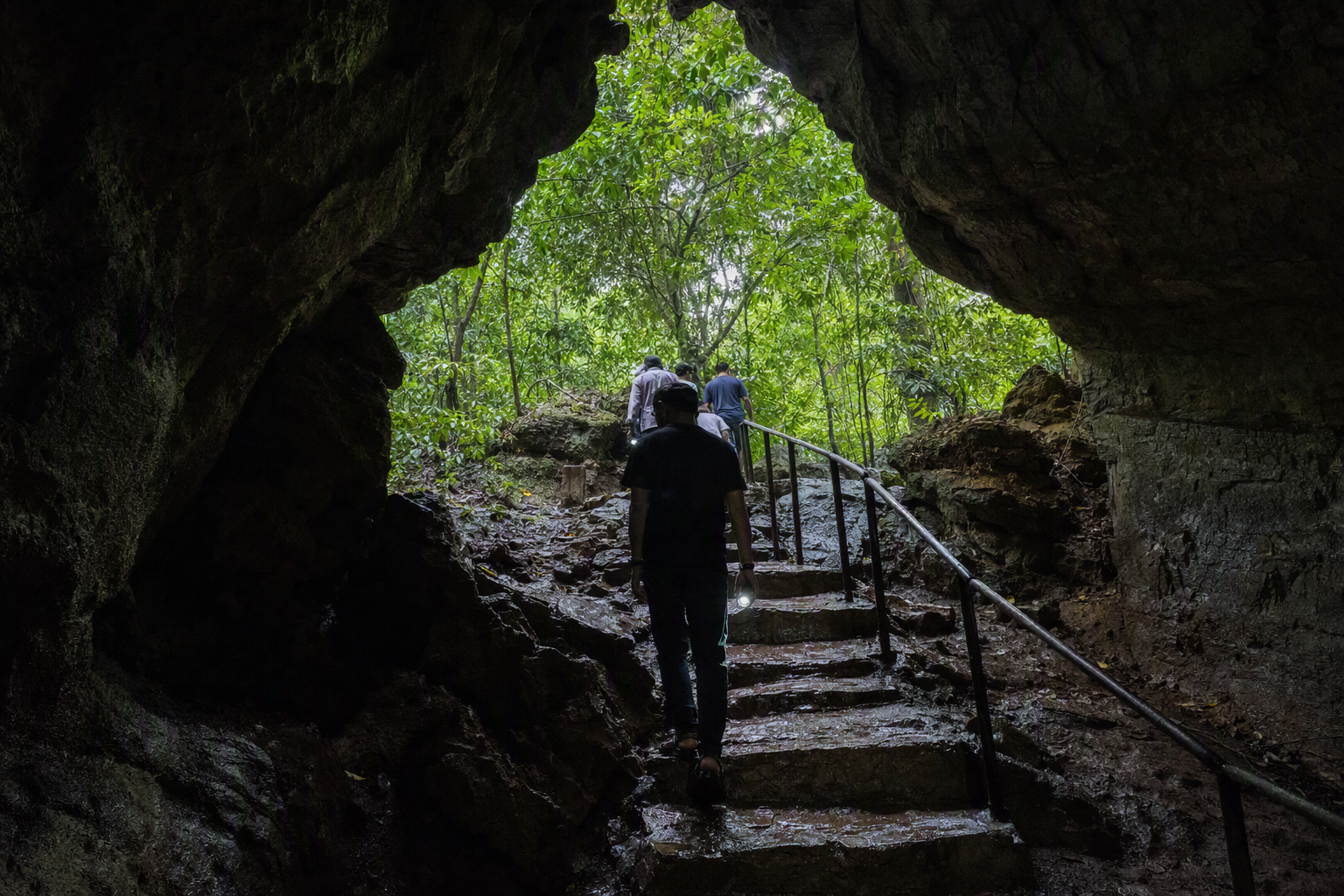 The forested entrance and dark stone passage of Alutila Cave